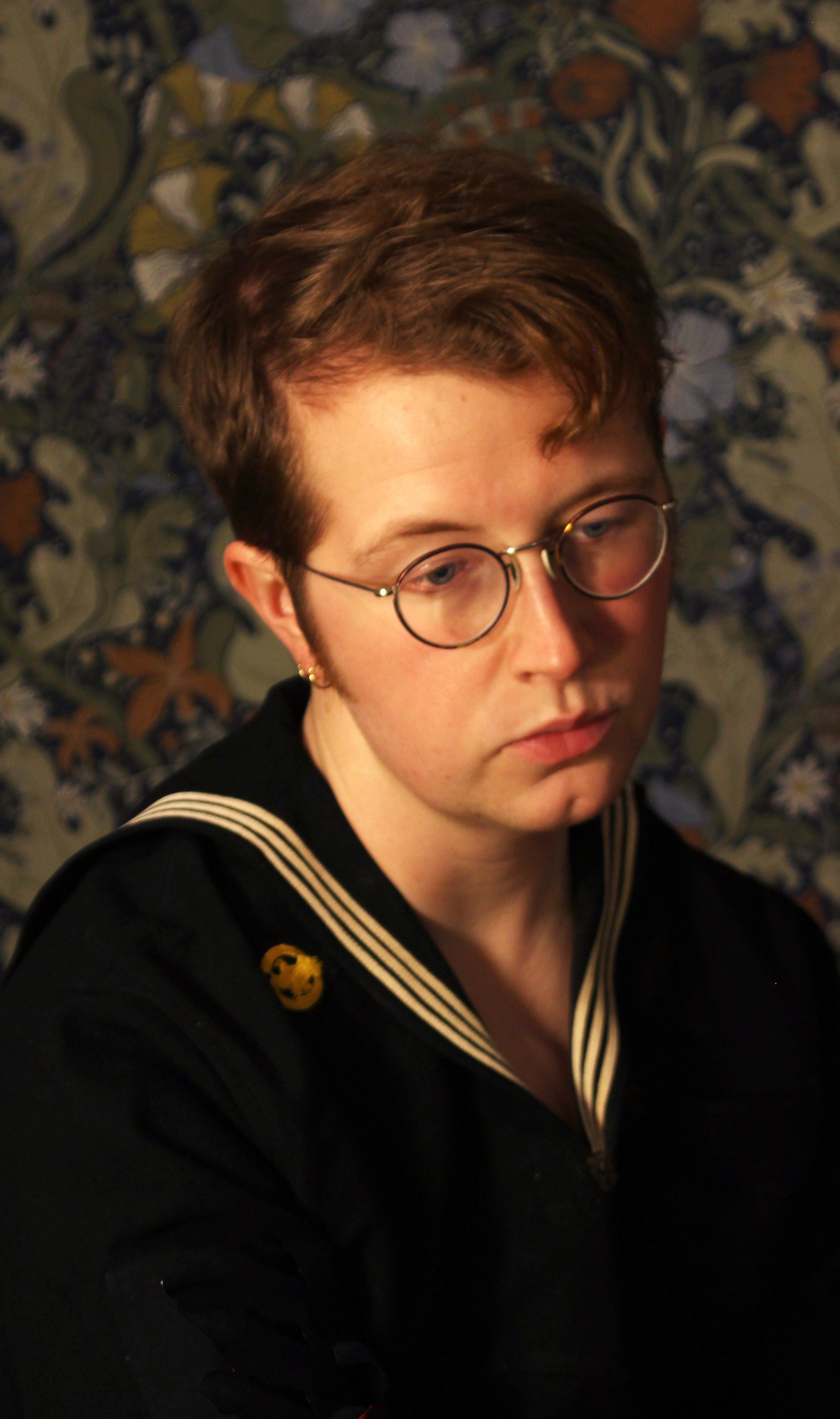 Photo of Artur, a young man with short brown hair and neat round glasses wearing a sailor shirt, in front of a botanical wallpaper.