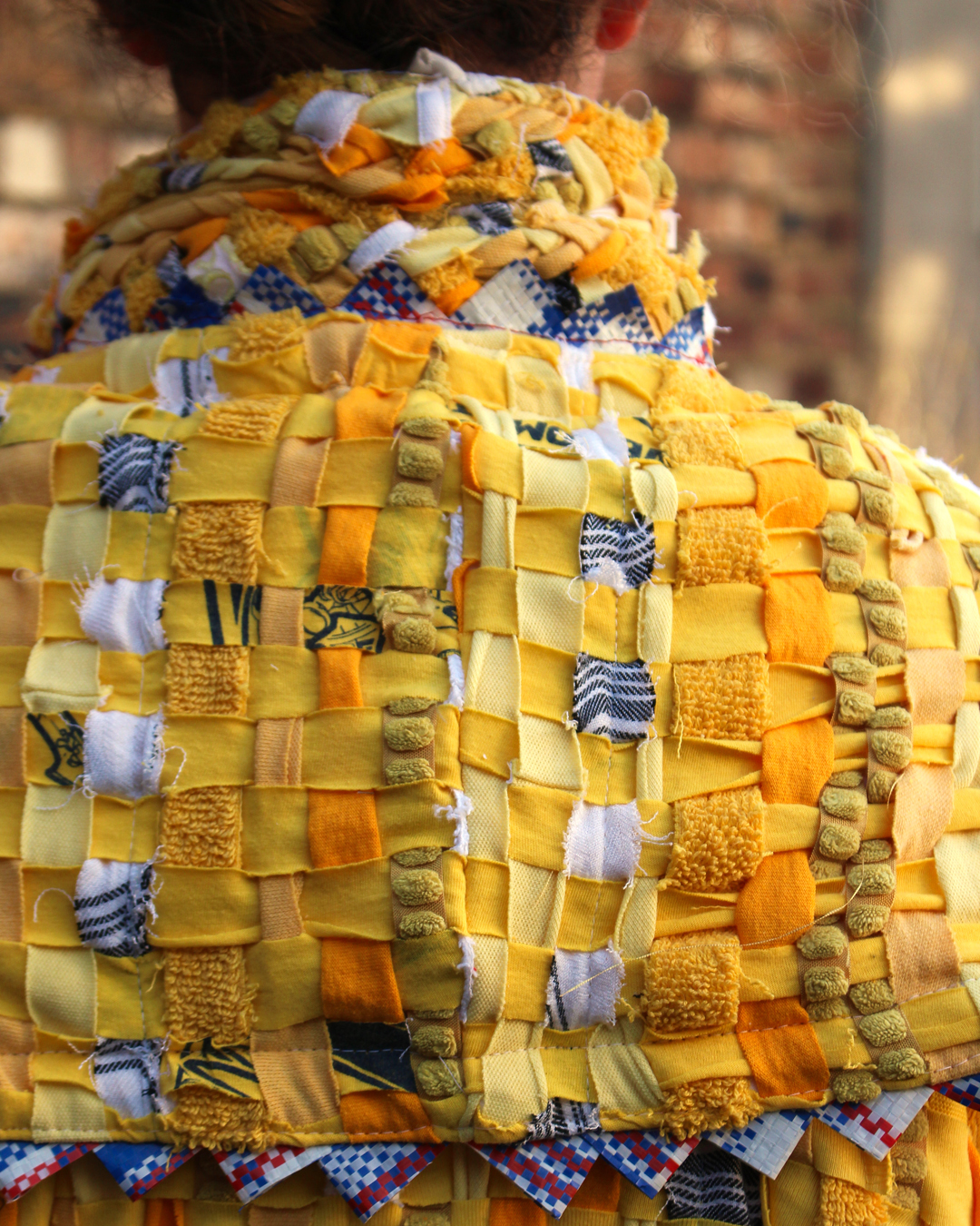 A close up photo of the back of the character, showing the woven rags and the zig-zag trim, as well as the standing collar.