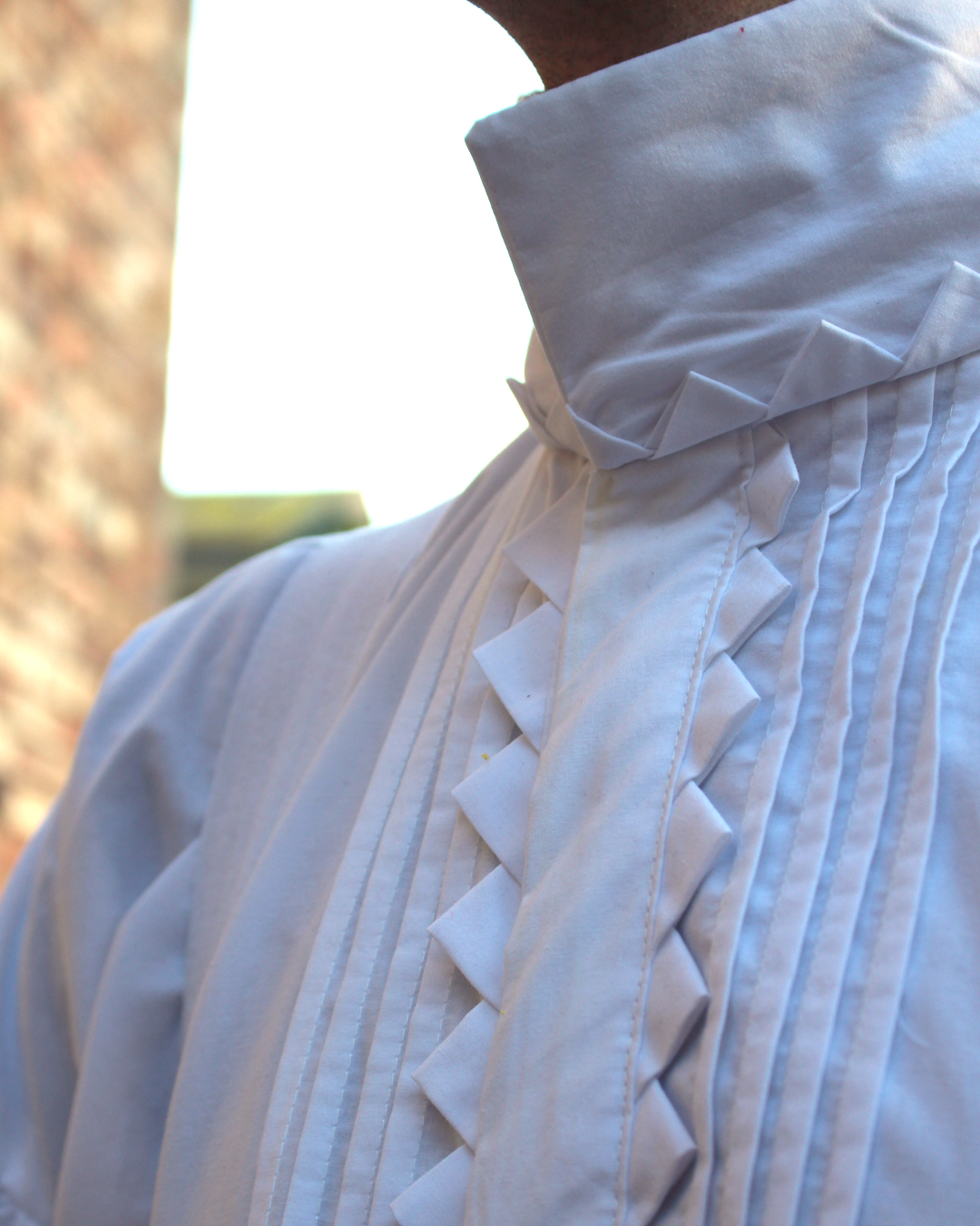 A close up photo of the under shirt. A white shirt with a hidden button closure and the same sort of zig-zag trim along the button placket, but this time in white fabric. The collar is a square standing up.
