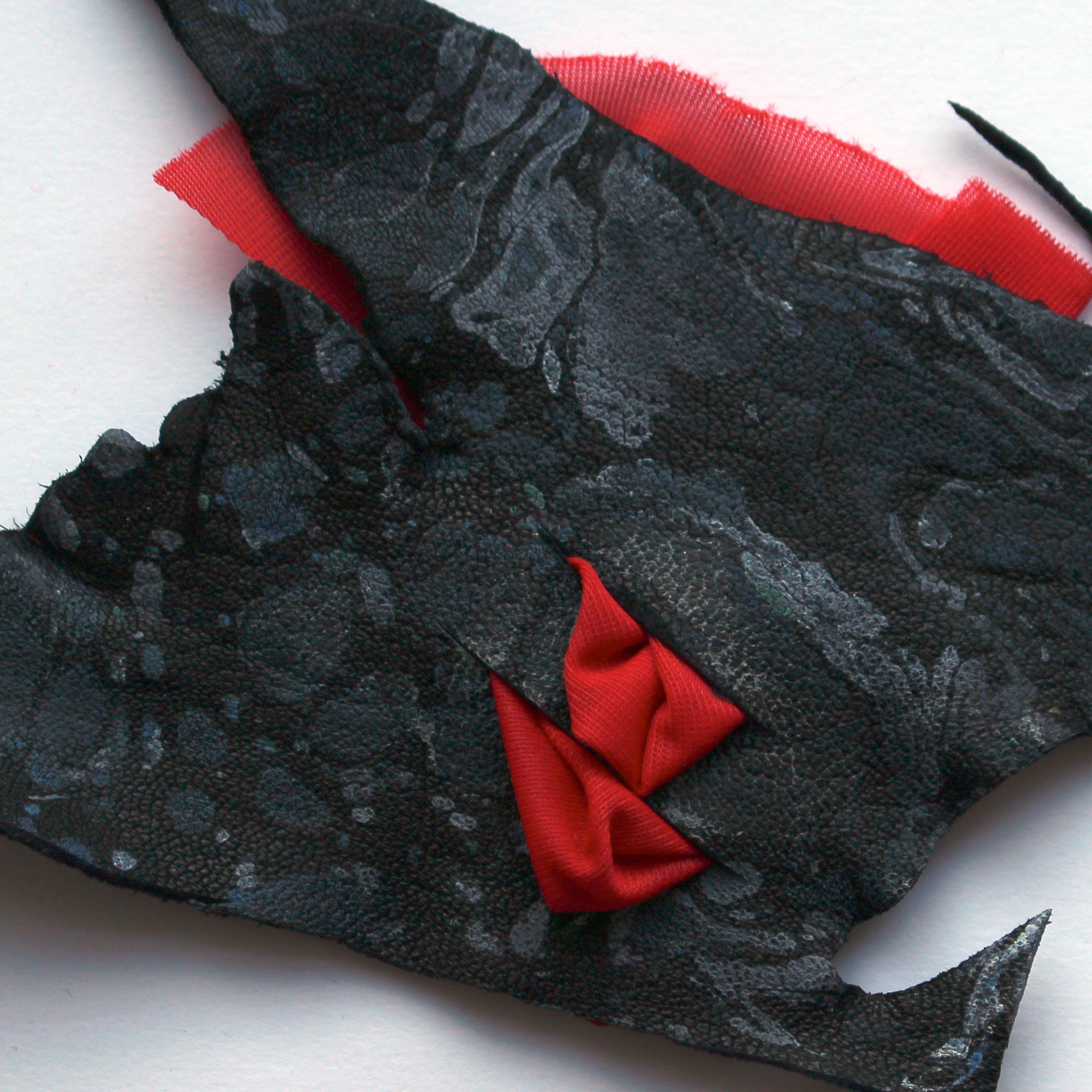 A photo of a material sample: a piece of black leather with white marble surface detailing and red fabric puffing out through three slashes.