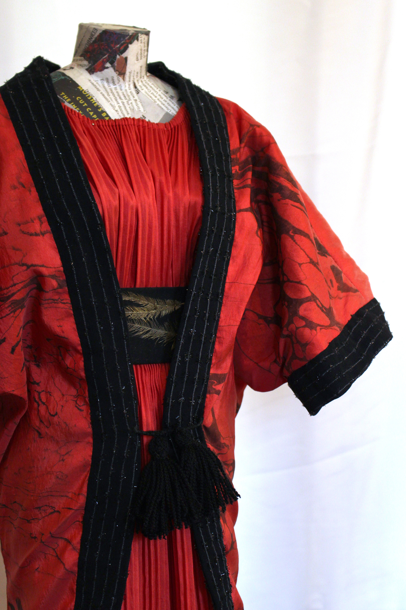 A waist-up photo of the red taffeta dress and the opera coat. This angle shows the V-line of the front hem of the opera coat, and the glitter detail of the black fabric edge.