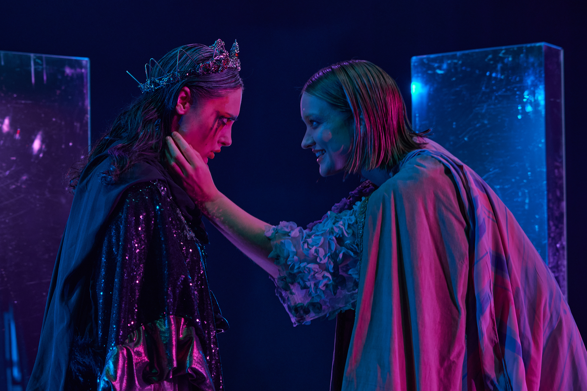 The same image as the thumbnail: a photo of two actors facing each other. Tintomara, the actor on the right, is smiling and holding the face of Clara between her hands. Clara frowns, her make up smeared and a crown on her head.