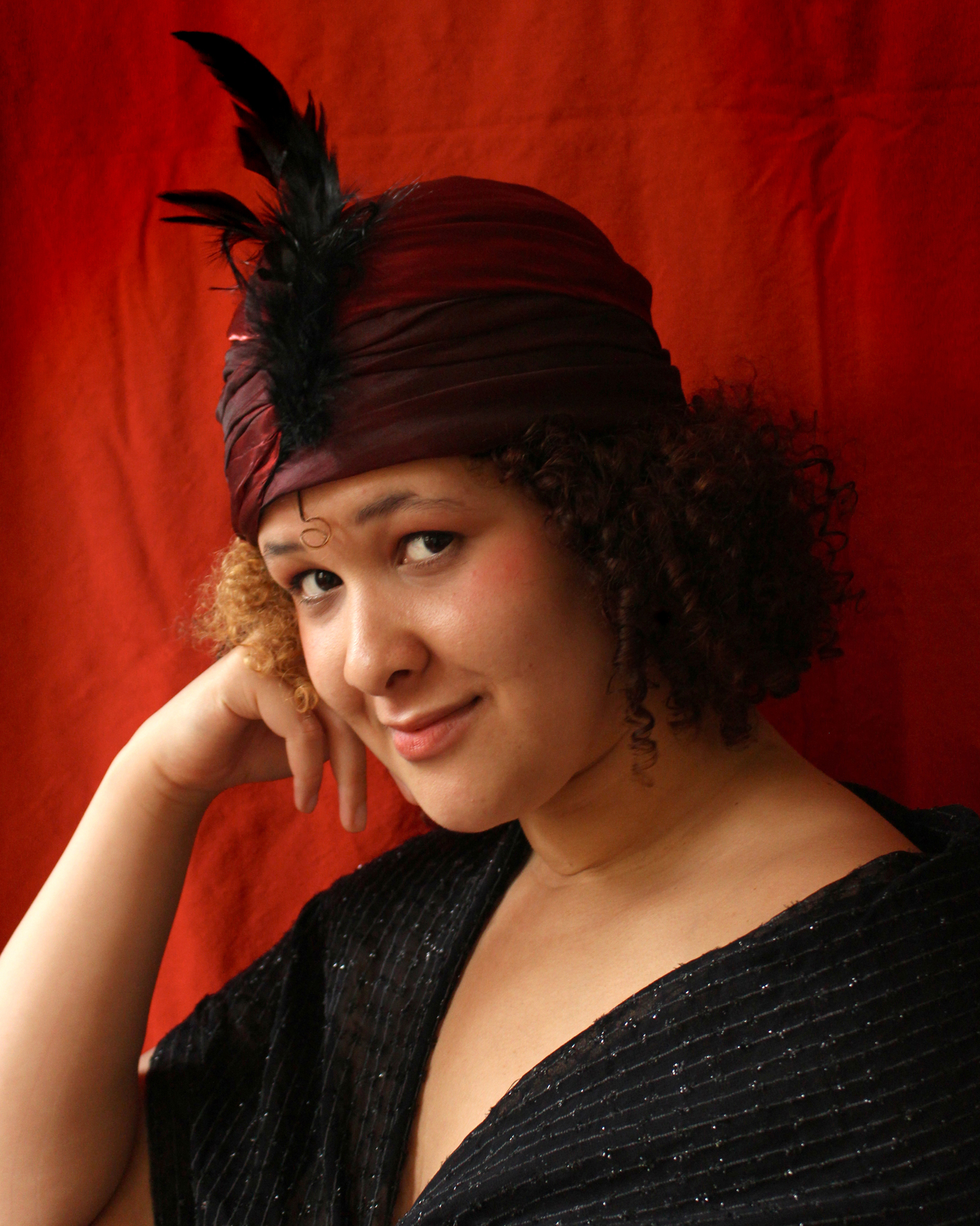 Ett porträttfoto av en modell bärandes en röd turban med fjäderdekoration.