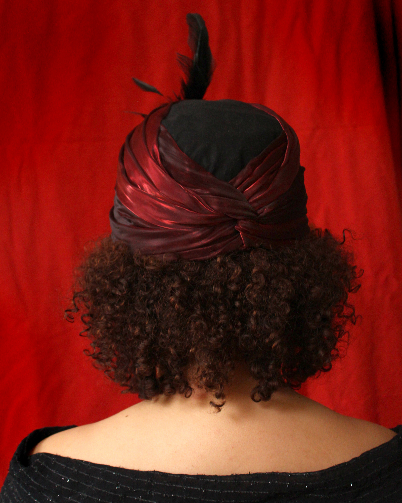Ett porträttfoto bakifrån av en modell bärandes en röd turban med fjäderdekoration.